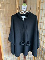 Front view of black hooded cashmere poncho with fur ties on hanger