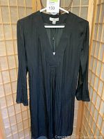 Front view of black Halston tunic top hanging on white hanger against wood backdrop showing front of the garment including deep V-neck and long sleeves.