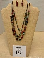 Full view of necklace and matching earrings displayed on a beige bust stand, showing multicolored glass beads and antiqued bronze chain detail with red drop earrings.