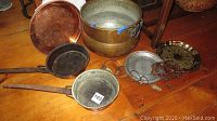 Copper cookware and serving items displayed on wooden floor, showing all items including pot, pans, trays, and bell.