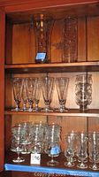 Shelves showing multiple pieces of Princess House glassware including dessert cups, glasses, and vases with floral etched patterns.