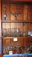 Photo showing two tall single flower vases and a large footed bowl on the top shelf, with multiple glasses, cocktail glasses, dessert bowls, covered butter dish, and salt and pepper shakers on lower shelves.