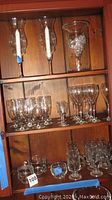 Glassware set displayed on wooden shelves including tall candle holders, stemware, mugs, and decorative container with silver items