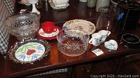 Photo showing multiple bowls including clear cut crystal and a colorful floral decorative plate on a table.