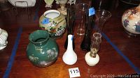 Photo showing four items: a 10-inch green floral vase with chip, 8-inch white textured vase, 8-inch oil lamp, and clear glass vase.