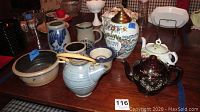 Photo showing three teapots, Chester County canister, stoneware bowls and pitchers arranged on wooden table.