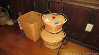 Two Longaberger baskets with wooden lids housed in a black metal snowman-shaped holder on wooden floor.