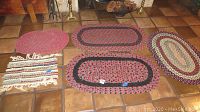 Photo showing five small rugs and mats of different styles and colors on tiled floor.