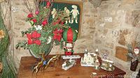 Wide view showing faux flower display, metal deer figurines, pine cone village, Santa in balloon, and other holiday decorations on wooden furniture.