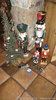 Photo showing large and medium-sized nutcracker figurines with the Christmas tree decorated with mini nutcracker ornaments, wooden floor and stone wall background.