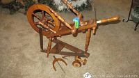 Full view of wooden spinning wheel with a large wheel, frame, and several pieces including a flyer and wooden bobbin laid out beside it on carpeted floor.