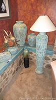 Photo showing the full set placed on stone ledge with rustic background including three vases and the lamp among floral decoration.