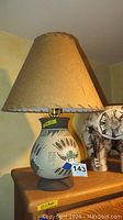 Side view of southwestern style handcrafted pottery lamp base with geometric and symbolic sand art painting and tan stitched fabric shade.