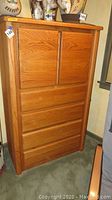 Full view of oak chest of drawers with 4 drawers and 2 sliding doors. Shows wood grain finish and overall height.