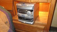 Photo of GPX stereo unit placed on wooden furniture, showing front panel with 3 CD player slots and control buttons.
