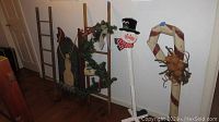 Wide shot showing all decorations including ladder, sled with snowman design, standalone snowman figure, and candy cane decoration.