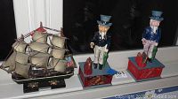 Photo showing two Uncle Sam mechanical banks and one model ship placed on a windowsill with reflective glass background.