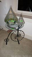 Full lot photo showing metal bicycle base table with glass top and two glass terrariums placed on top.