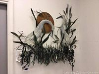 Metal wall art mounted on wall featuring two white birds, green reeds, and a round copper sun behind.