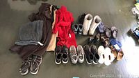 Full view of all coats and shoes laid out on floor including boots, sneakers, sandals, coats, and scarf