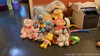 Wide view of the collection of plush stuffed animals arranged on the floor, including large and small bears, colorful plush toys, and various animal characters.