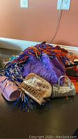 Pile of assorted colorful pom-poms, purple fuzzy doll clothing, doll shoe accessories, and sparkly purses