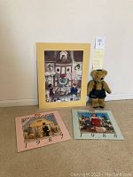 Lot showing 1987 and 1988 Steiff calendars and Jane's Originals Harrods teddy bear. Calendars have vintage Steiff animal scenes and texts in English and German respectively. Teddy bear wearing green shorts, suspenders, bow tie, and hat sitting next to calendars.
