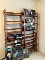 Two wood stacking shelves side by side with some books and picture frames on shelves, with some art and objects on floor beside them.