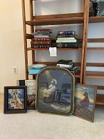 Wide view of shelves with Bibles stacked, porcelain prayer bowl on middle shelf, three framed Christian images and wooden inspirational sign leaning against shelf.