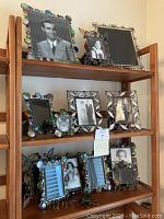 Photo showing 13 assorted stained glass picture frames arranged on wooden shelves, various sizes and designs, some with black and white photos.
