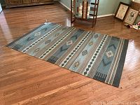 Full view of rug laid flat on hardwood floor showing overall pattern and fringe.