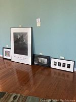Four framed artworks displayed on the floor against a wall, including a large Andrew & Jamie Wyeth museum photo, a bird photo, a daisies print, and a colorful watercolor