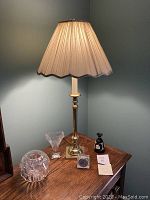 Brass lamp with cream pleated shade illuminating on a wooden surface along with crystal rose bowl, Waterford crystal vase, Wedgwood jasperware bud vase, and small clock.