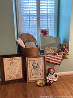 Lot displayed on window seat includes round wooden sewing box with pillows, framed samplers, Raggedy Ann doll, Americana themed teddy bear and folded fabric flag decor