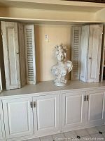 Monticello lady bust centered between two rustic white wooden shutters placed on built-in shelving.
