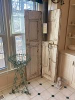Full view of the painted green metal wire plant stand, rustic distressed wood shutter, and small plaster angel on floor in front of shutter.