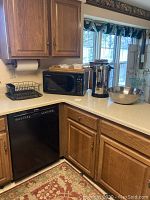 Kitchen countertop with Panasonic black microwave, black dish drainer, Nesco hot water heater, and large stainless steel mixing bowl.