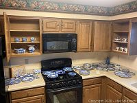 Overall shot of blue and white china pieces arranged on kitchen counter and stove, including cups in cabinet and plates and bowls spread out on countertop and stove.