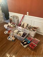 Multiple plastic storage bins containing assorted holiday ornaments, gift wrap roll, Christmas pillow, plates and gift bags