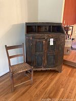 Rustic dark wood cabinet with two doors and upper compartments beside wooden chair with woven seat