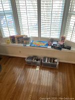 Overview of lot items on window sill and floor bins with DVDs and puzzles