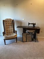 Full view of cane-sided wing chair, Singer sewing machine cabinet, and two small samplers placed on floor in front