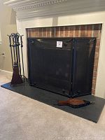 Fireplace screen positioned in front of a brick fireplace, accompanied by the matching wrought iron tool set and tools.