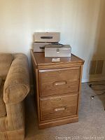 Photo of one oak 2-drawer file cabinet with three small metal lock boxes on top.