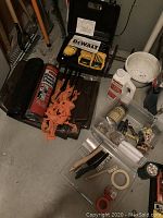 Photo showing Dewalt drill, drill bits and case, trash bags, orange saw, brushes and small tools placed on floor.