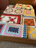 Five patchwork quilts laid out on a bed showing diverse patterns and colors including stars and geometric designs