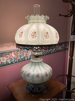 Photo of green Victorian style glass lamp showing floral designs, glass chimney, and ornate metal base