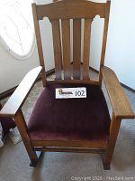 Front view of vintage oak rocking chair showing slatted backrest and dark maroon upholstered cushion with rivet trim