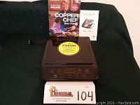 Photo showing the full induction cooktop with cookbook and owner's manual behind it, all placed on a dark cloth background.