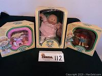 Three boxed Cabbage Patch Kids dolls: one Preemie doll in the center, and two Pin-Ups dolls on each side, all in original packaging.